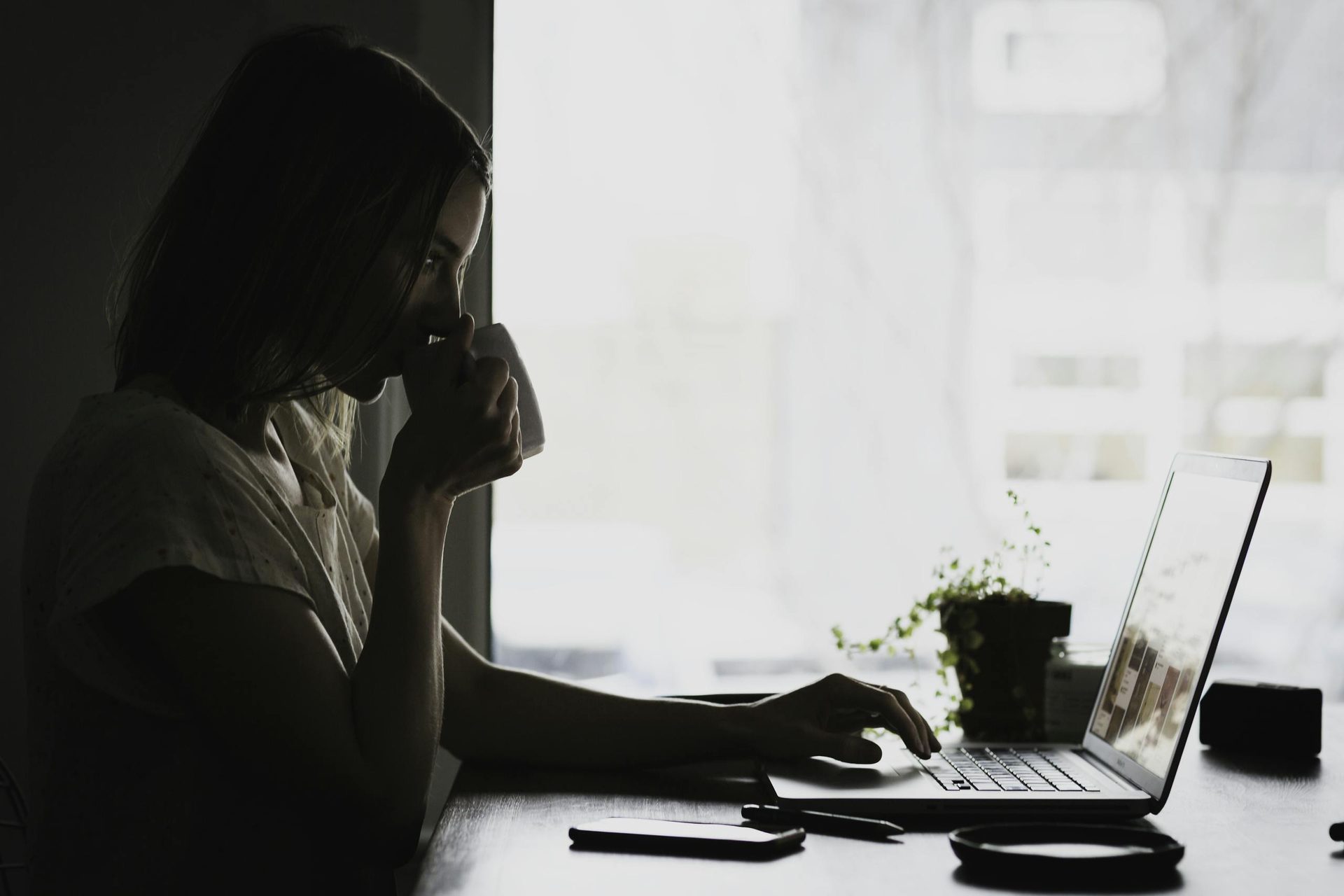 A businesswoman works remotely from home, sipping coffee and using her laptop.