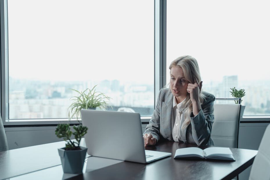 Professional woman engaged in a video meeting at a modern office desk with a laptop.