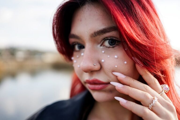 Detailed close-up of a woman with red hair, pearl adornments, and stylish nails.