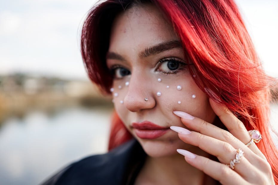 Detailed close-up of a woman with red hair, pearl adornments, and stylish nails.