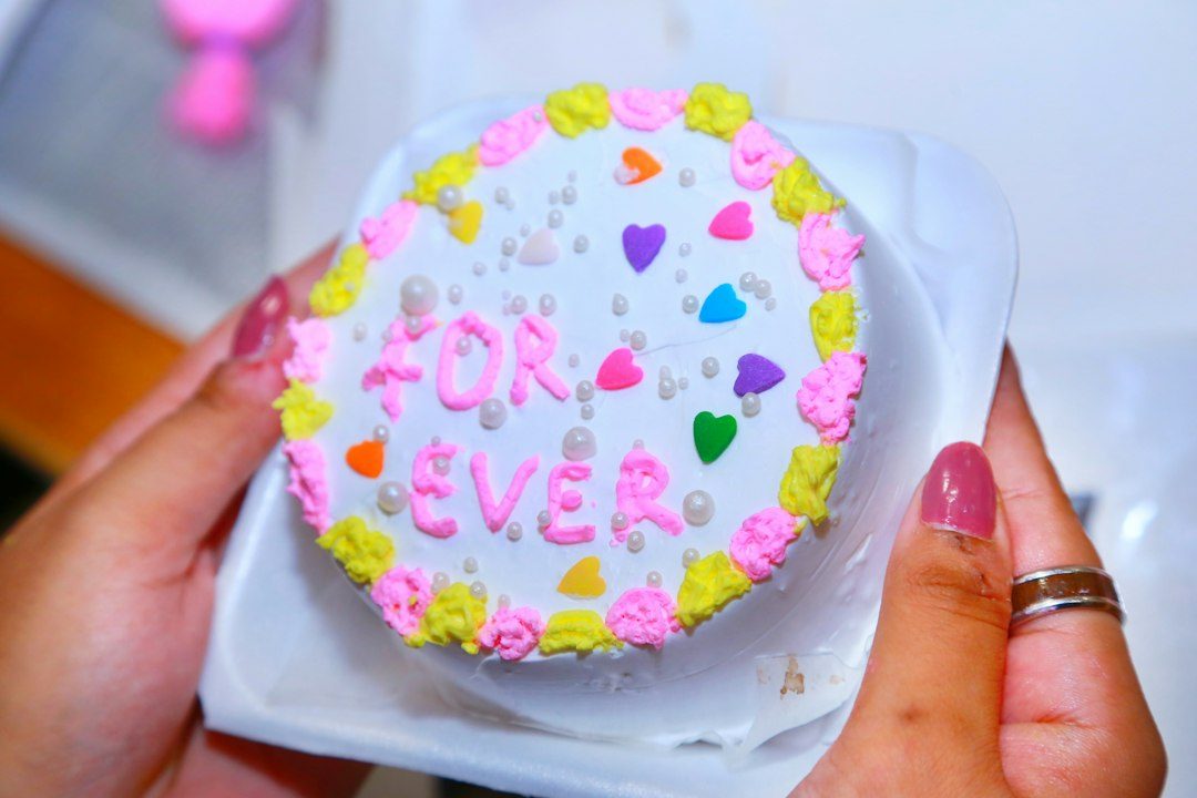 Hands holding a small cake decorated with hearts. Imagem ilustrativa para Bento Cake Dia dos Namorados: O Bolo Pequeno que Transborda Amor.