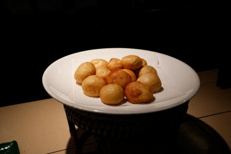 A white plate filled with golden brown fried dough balls. Imagem ilustrativa para Bolinho de Chuva sem Ovo e sem Leite.