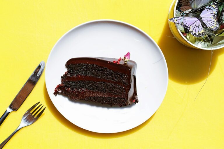 sliced chocolate moist cake in plate near gray stainless steel fork and knife. Imagem ilustrativa para Bolo de Chocolate com 3 Ingredientes.