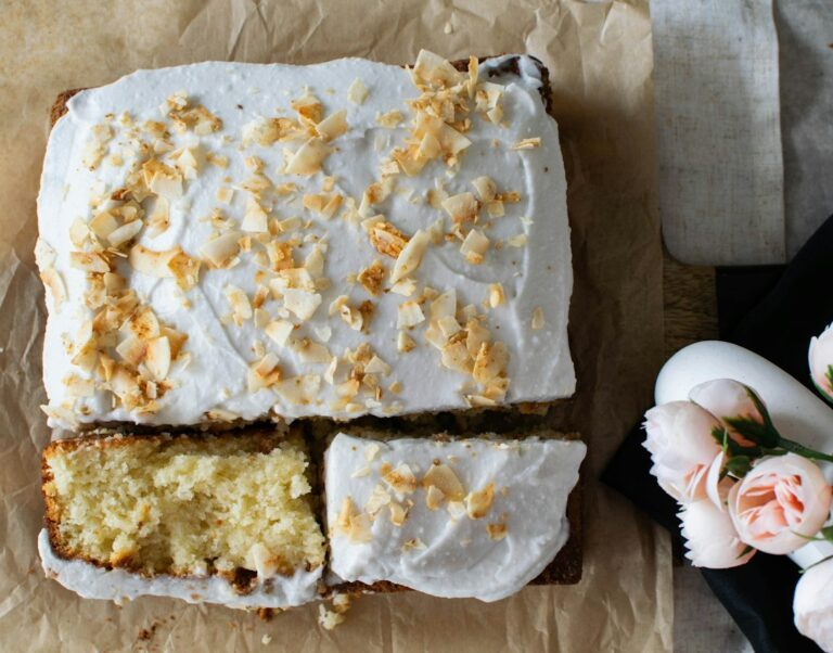 a close up of a cake with white frosting. Imagem ilustrativa para Bolo de Coco Gelado Simples e Bem Molhadinho.