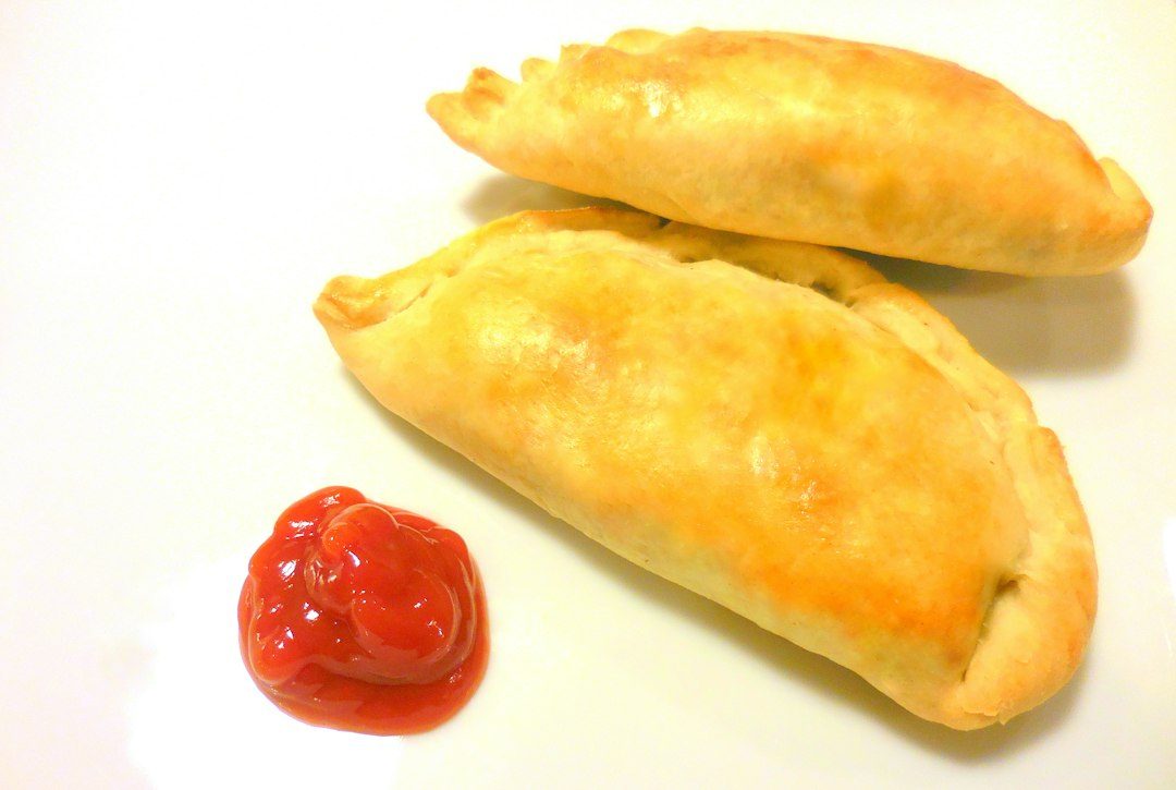 Two golden brown pastries with a dollop of ketchup. Imagem ilustrativa para Empada de Frango Caseira.