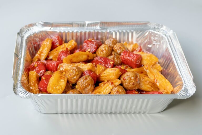 Meatballs, potatoes, and red peppers in a foil container. Imagem ilustrativa para Linguiça de Forno com Batata e Queijo.