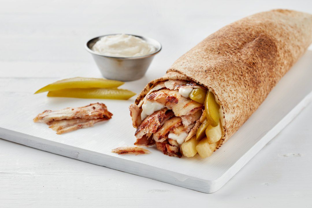 a burrito with a side of pickles and a small bowl of ranch dressing. Imagem ilustrativa para Wraps de Frango com Alho e Queijo: Sabor, Praticidade e Nutrição.